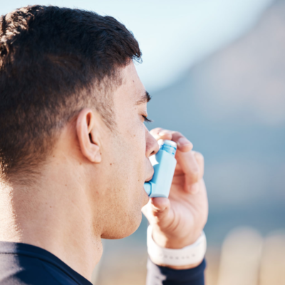 Person standing outdoors using an inhaler for asthma